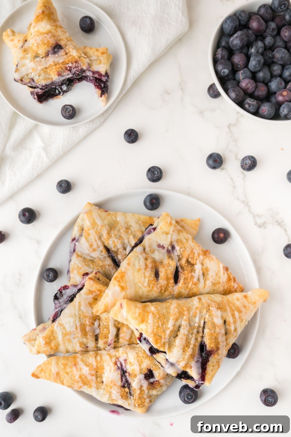 A vibrant overhead shot of a plate brimming with golden blueberry turnovers, accompanied by a scattering of fresh berries on the side, creating an inviting presentation.