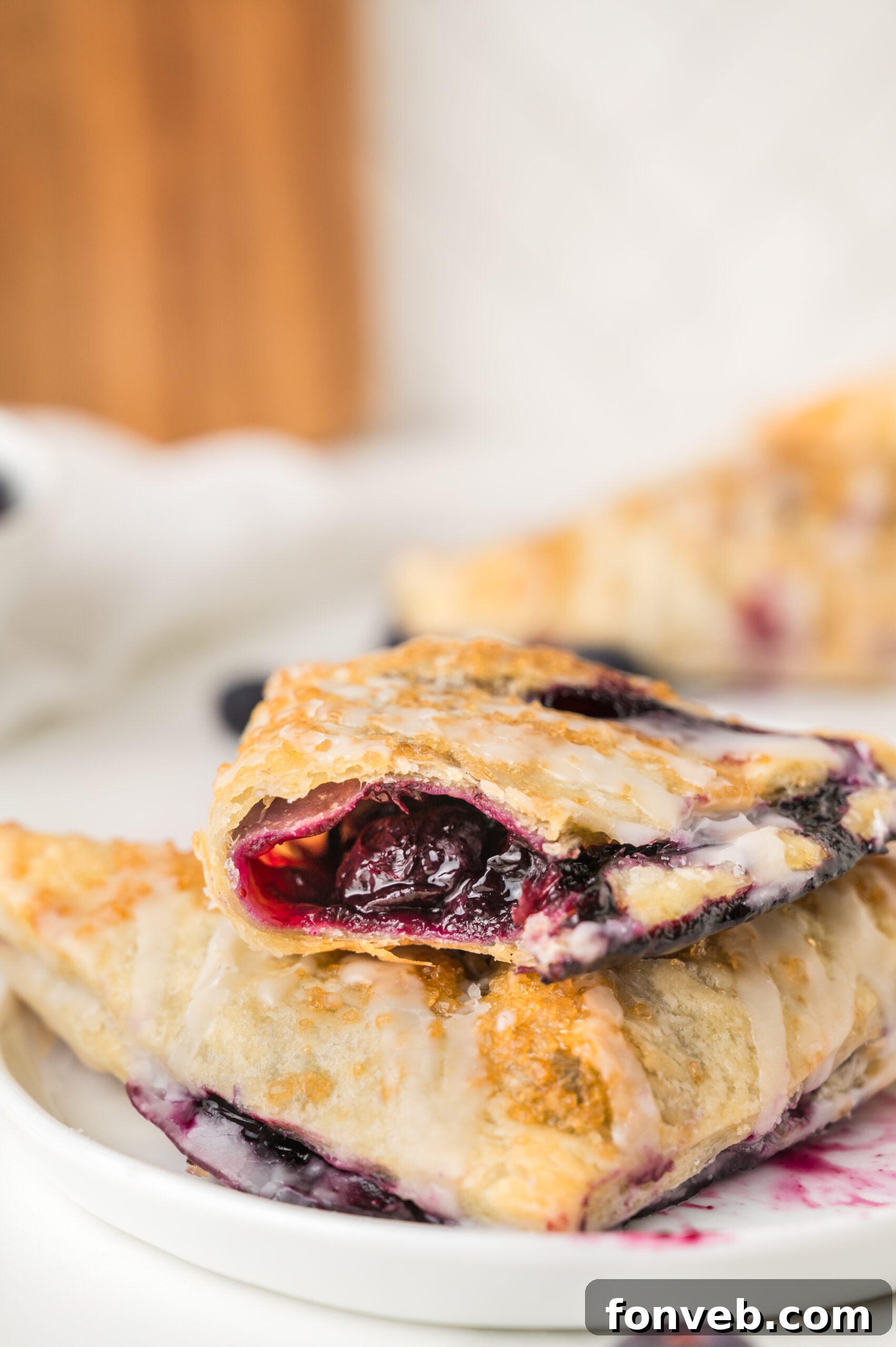 A blueberry turnover on a plate, with a bite missing, generously drizzled with white icing, highlighting its irresistible appeal.
