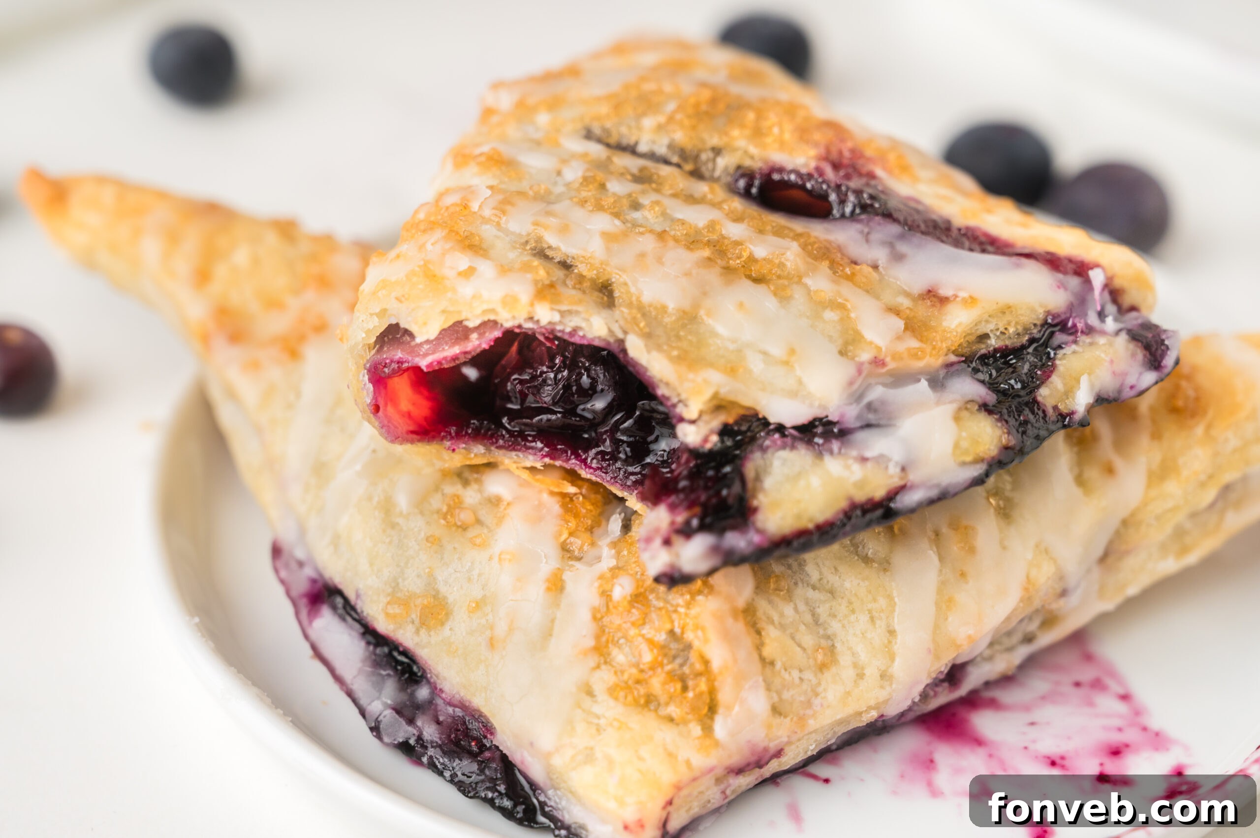 A close-up side view of a blueberry turnover on a plate, revealing its flaky layers and the enticing blueberry filling, showcasing its homemade perfection.