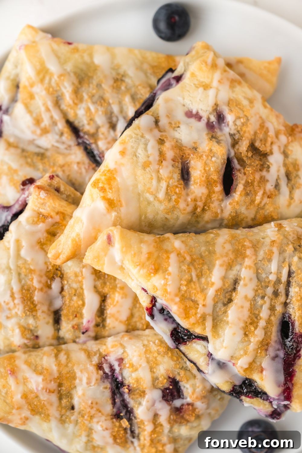Several blueberry turnovers neatly stacked on a plate, showcasing their impressive height and flaky layers, ready to be enjoyed.