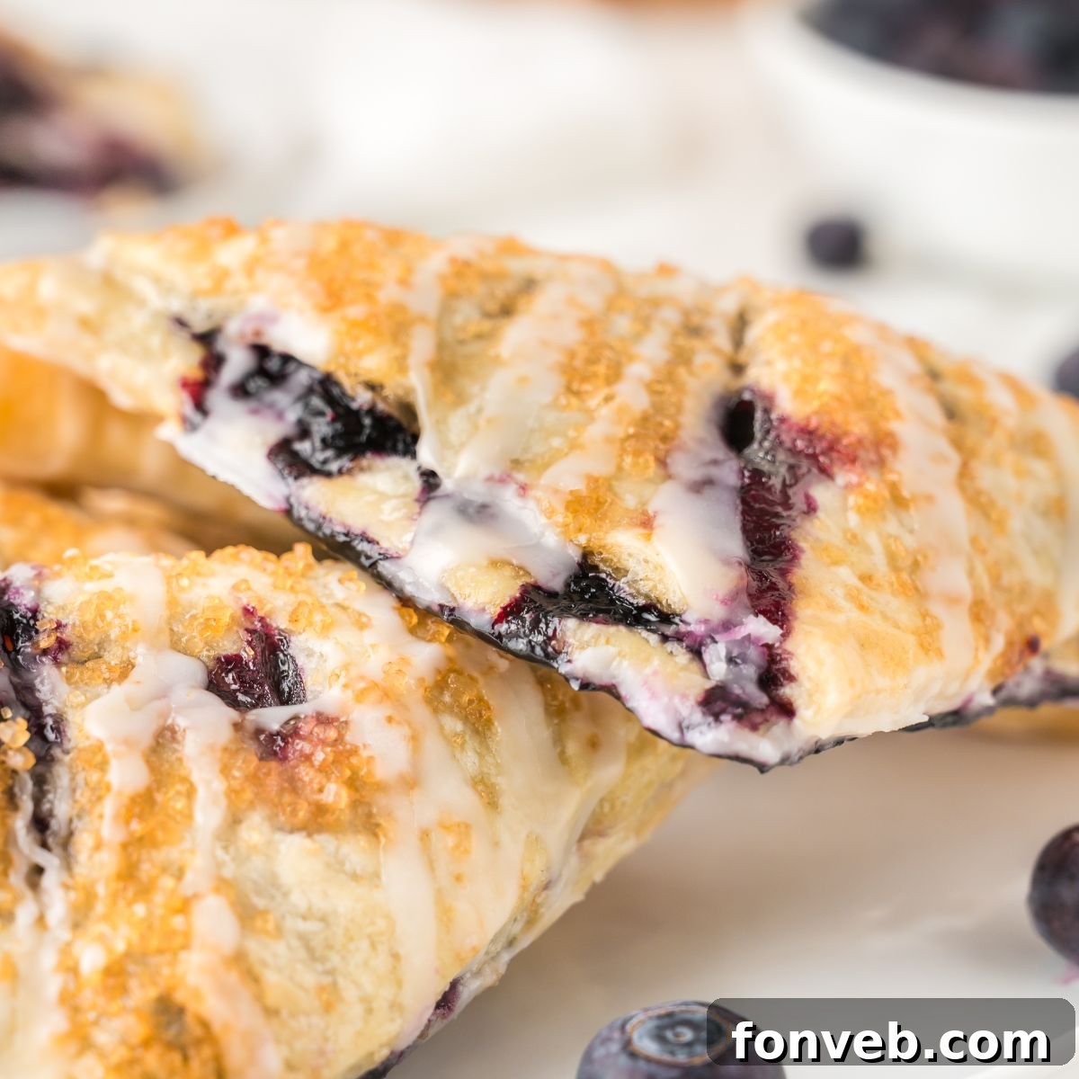 Close-up of golden blueberry turnovers on a plate, garnished with fresh blueberries, highlighting the beautiful texture and inviting warmth of the pastry.