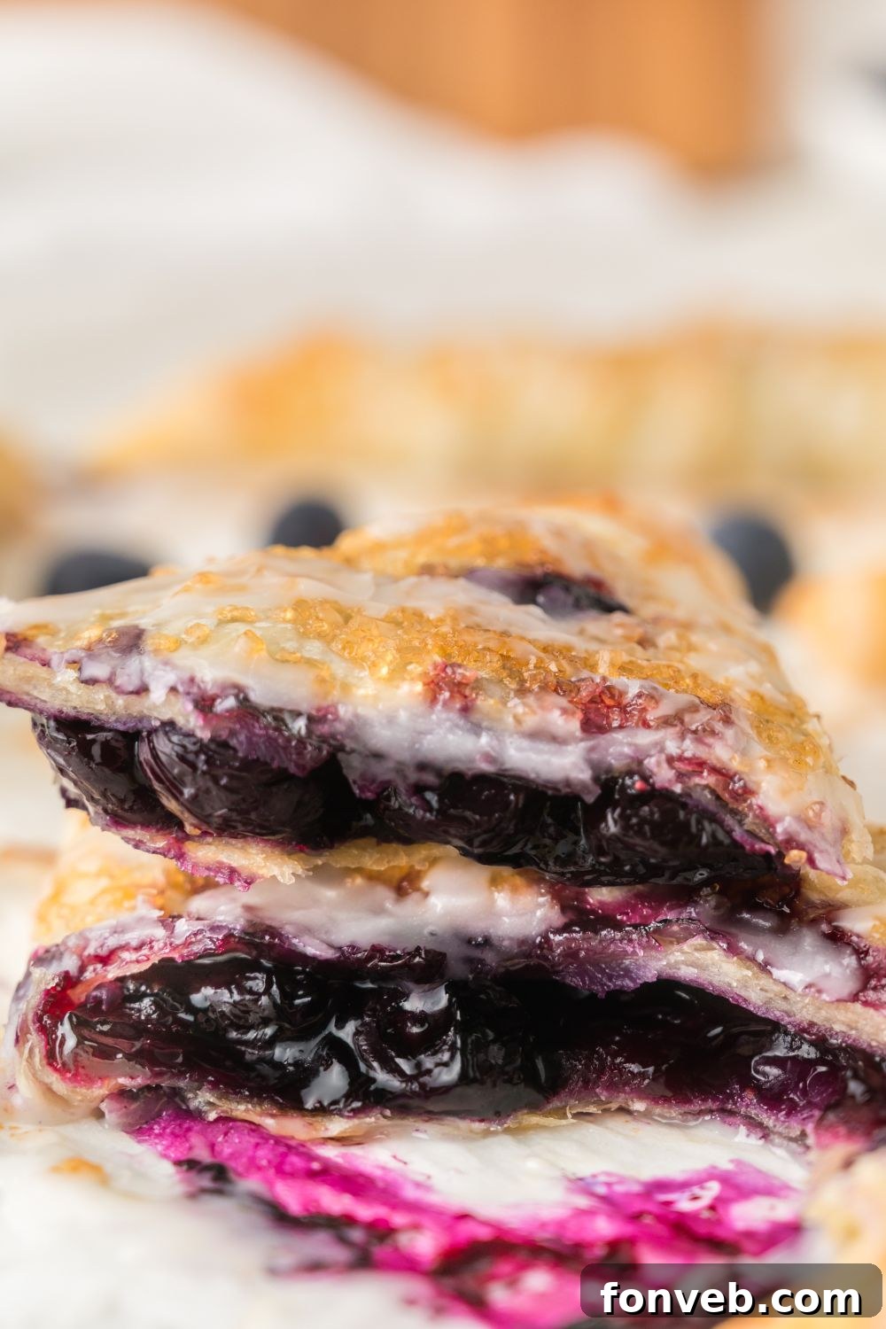 Blueberry turnovers sliced in half and attractively stacked, showcasing their generous fruit filling and perfectly golden, flaky pastry.