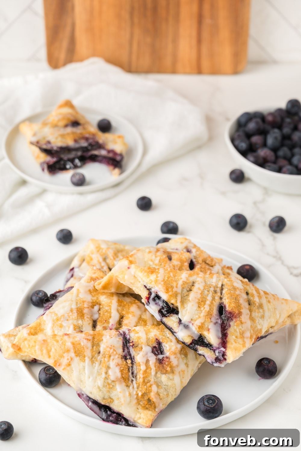 A serene display of blueberry turnovers on a rustic plate, surrounded by fresh blueberries scattered on a wooden table, evoking a cozy breakfast or tea time scene.