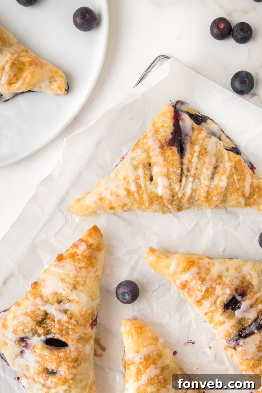 Unbaked blueberry turnovers neatly arranged and spread out on a baking sheet lined with parchment paper, showcasing their triangular folds and ready for the oven.