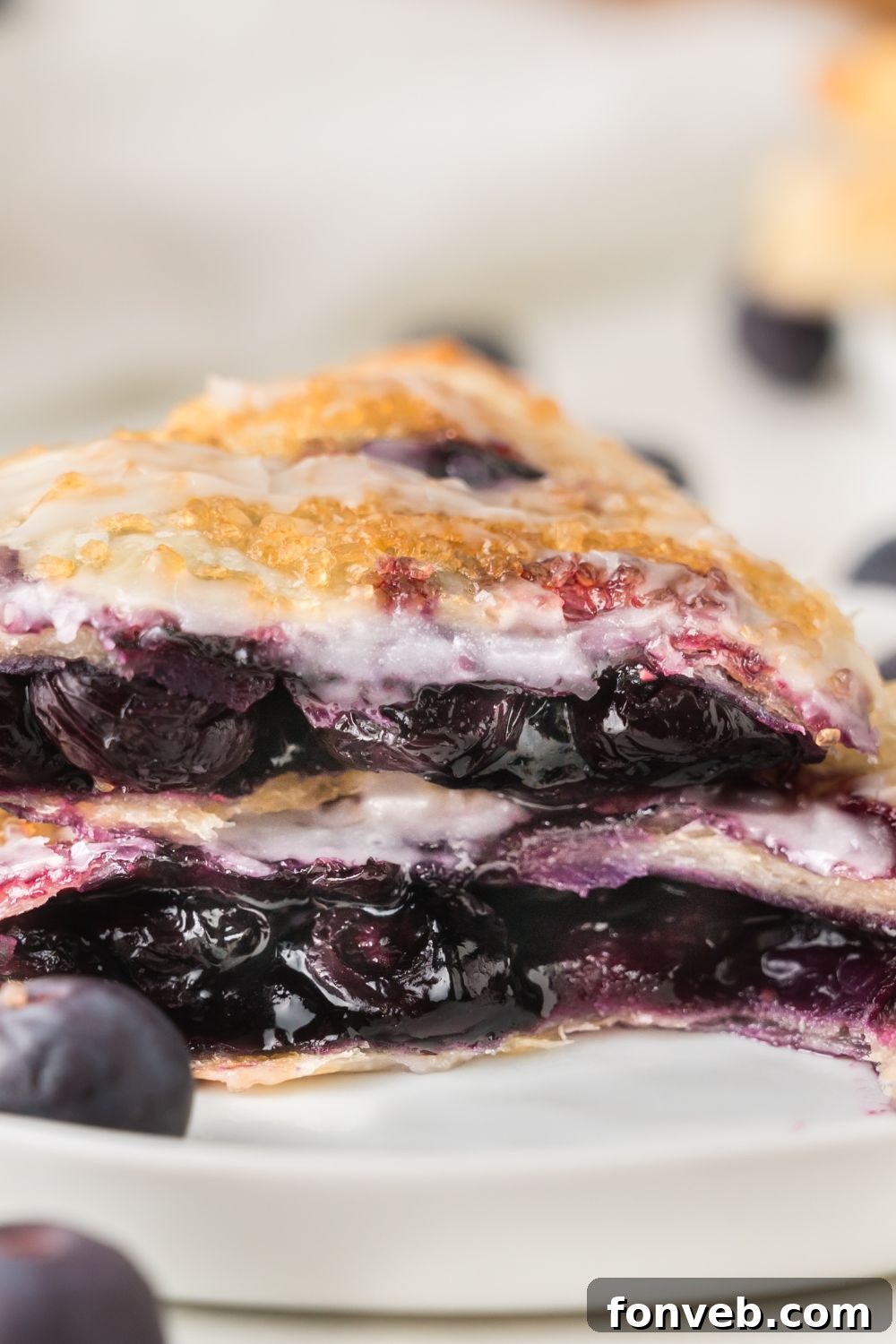 A blueberry turnover expertly cut in half, with the two pieces stacked to reveal the rich, purple blueberry filling encased within the golden, flaky layers of pastry.