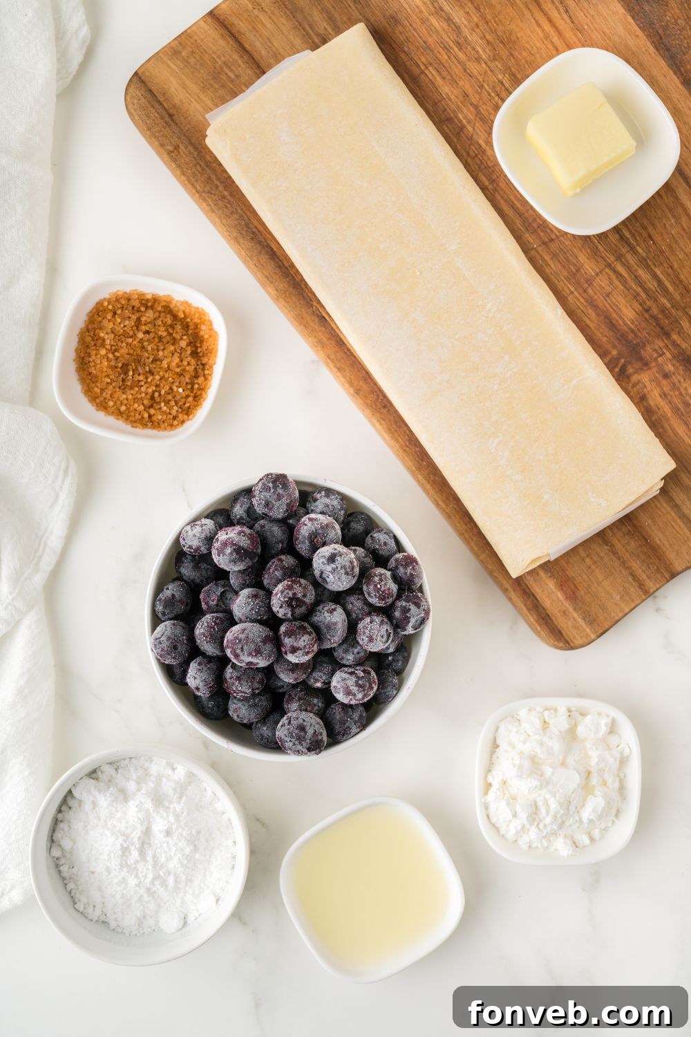 A collection of ingredients for blueberry turnovers, portioned in small individual containers, neatly arranged on a table to highlight each component for the recipe.