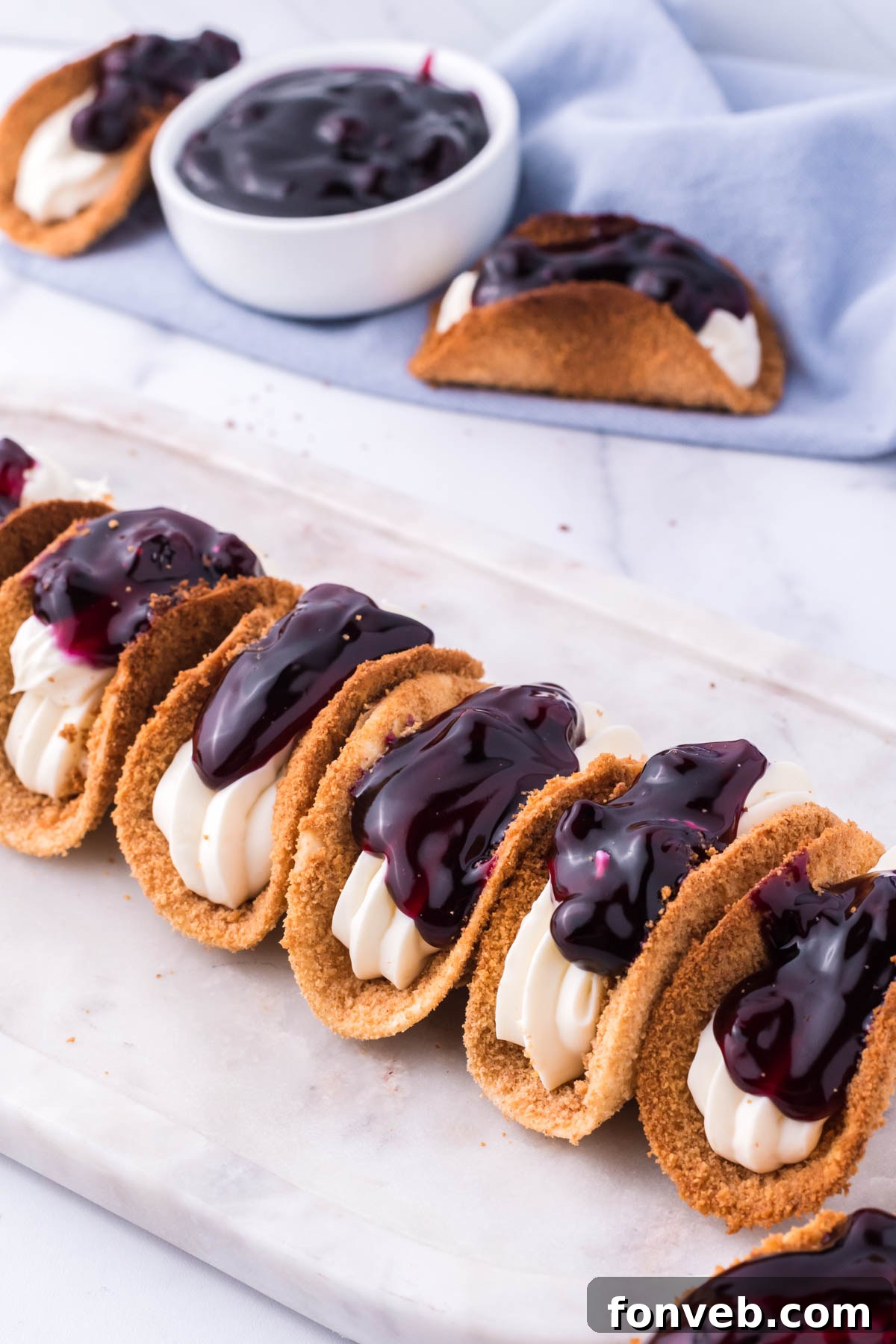 Blueberry Cheesecake Taco Twist 6 Photo of blueberry cheesecake tacos lined up on a marble serving platter.