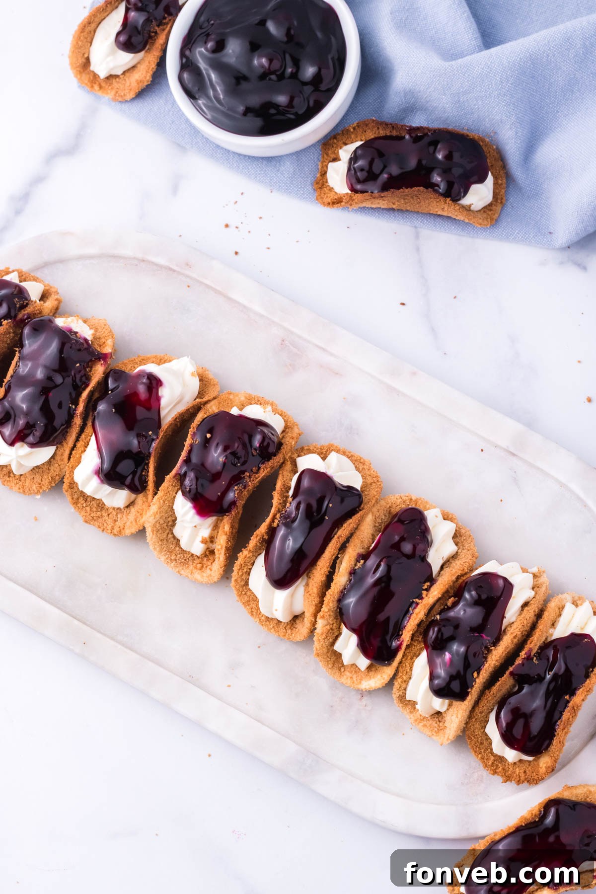 Blueberry Cheesecake Taco Twist 9 Overhead view of blueberry cheesecake tacos lined up on a marble serving platter.