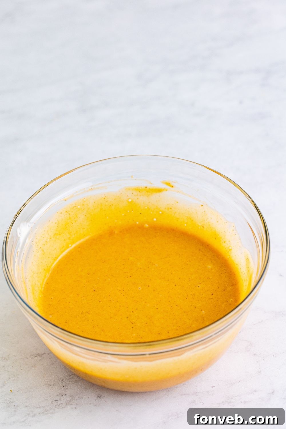 Close-up of the honey roasted BBQ sauce, freshly mixed in a glass bowl on a wooden table.