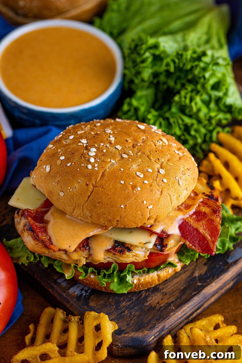A Chick-fil-A style grilled chicken sandwich presented on a wooden platter, surrounded by crispy fries and a small bowl of dipping sauce.