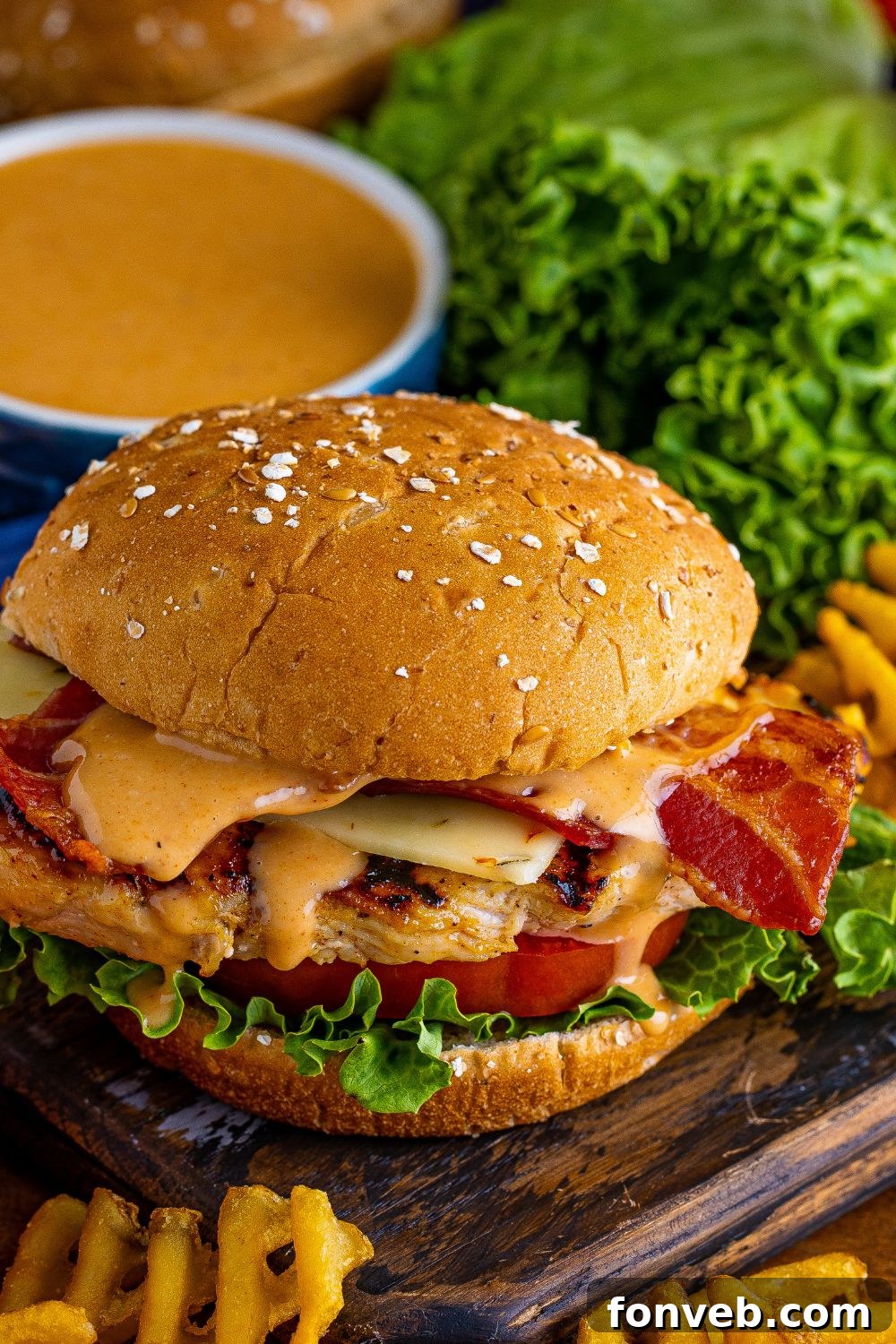 Close-up detailed view of a Chick-fil-A style grilled chicken sandwich, showcasing the tender chicken, crispy bacon, and fresh lettuce, with fries scattered around.