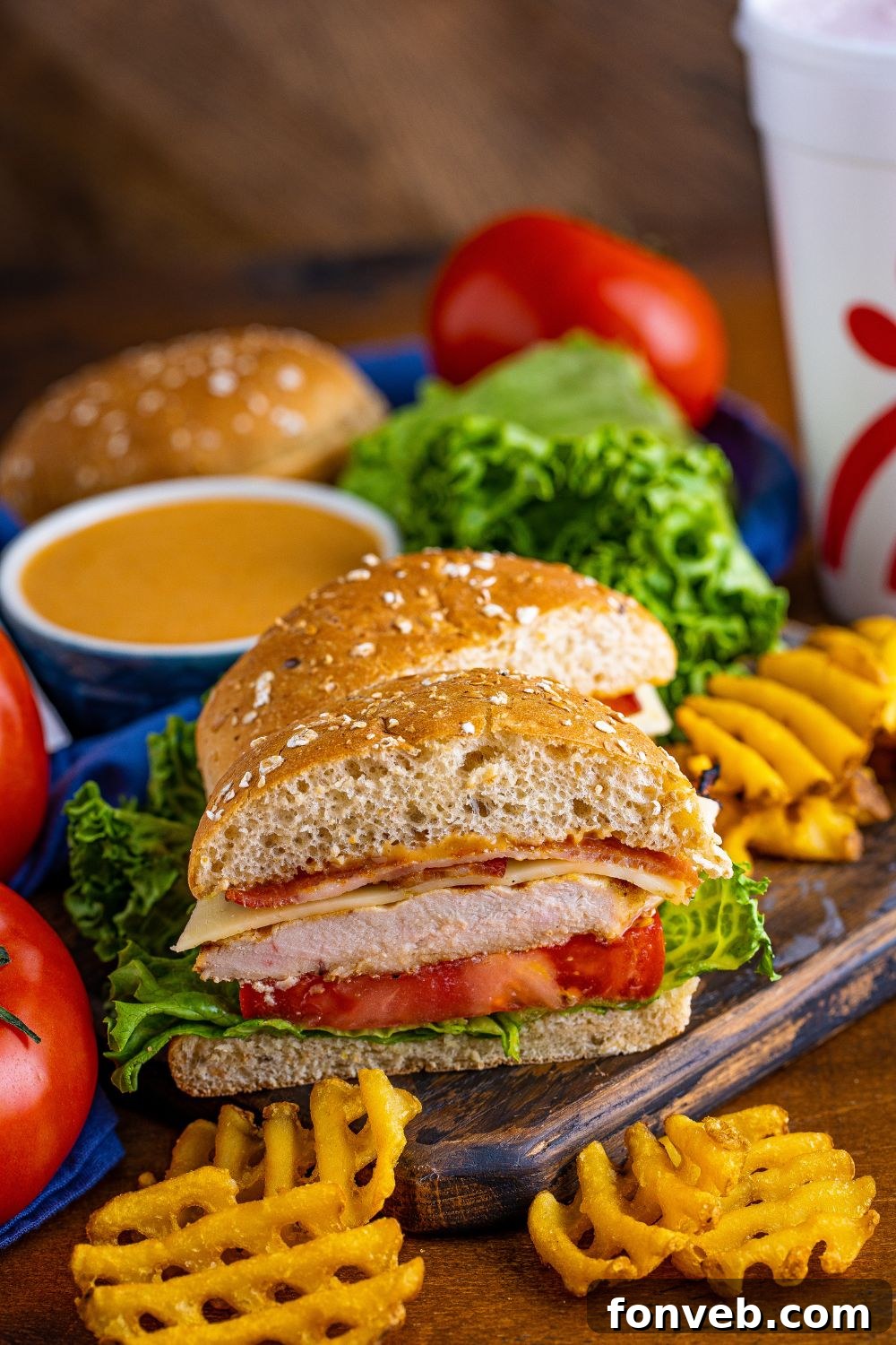 A perfectly sliced Chick-fil-A style grilled chicken sandwich revealing layers of chicken, cheese, bacon, lettuce, and tomato, with a side of dipping sauce.