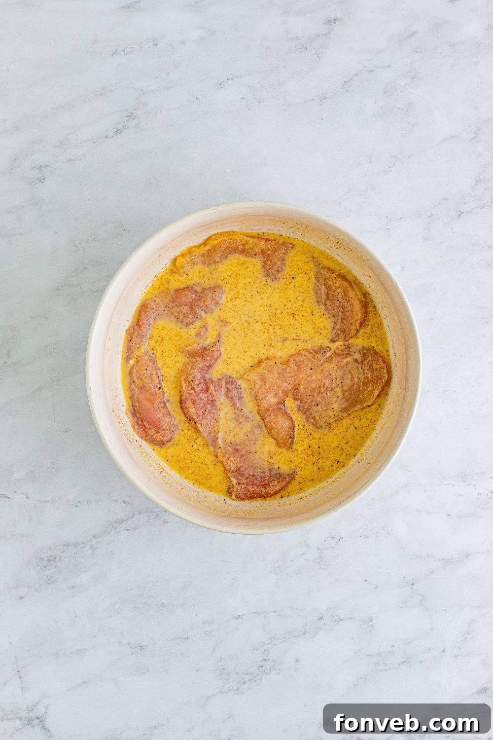 Chicken breasts marinating in a bowl with pickle juice and milk, preparing for a delicious grilled sandwich.