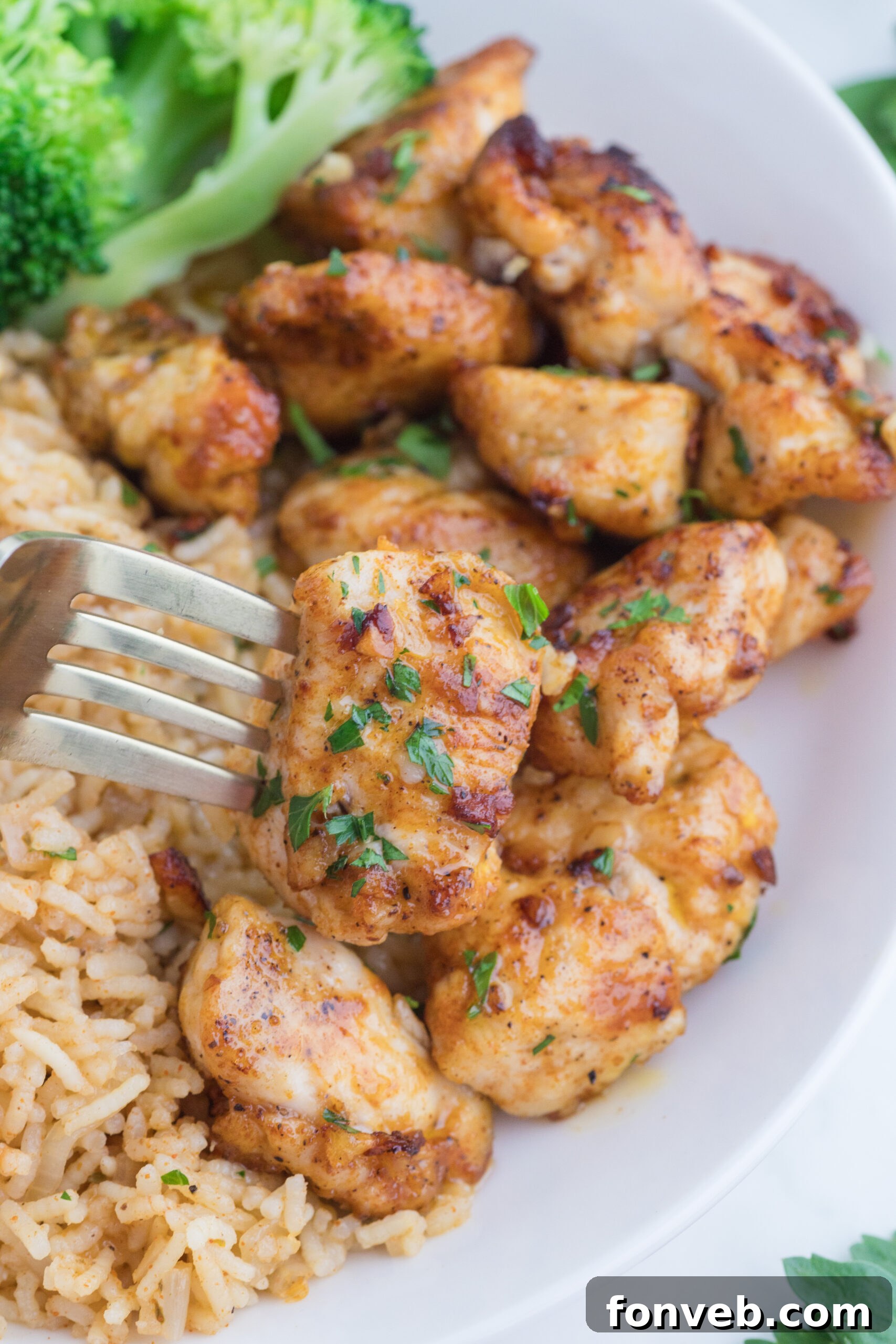 Garlic Butter Chicken Bites on a white plate with a fork lifting one up