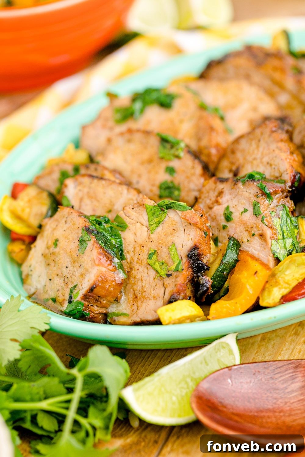 side view of platter full of cooked grilled pork tenderloin with limes and herbs around it