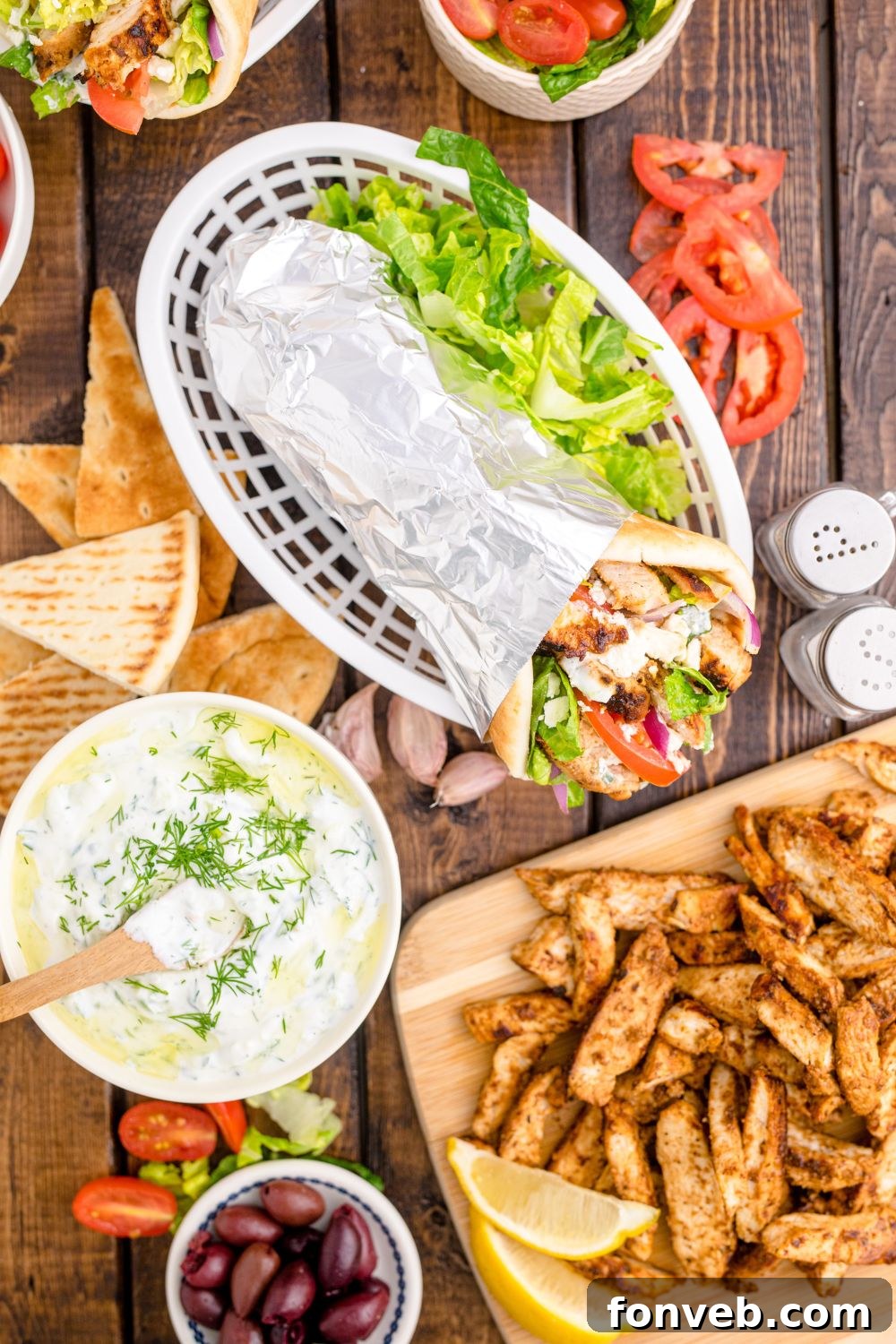 basket with gyros, bowl of tzatziki sauce in bowl, plate of diced chicken and more on table