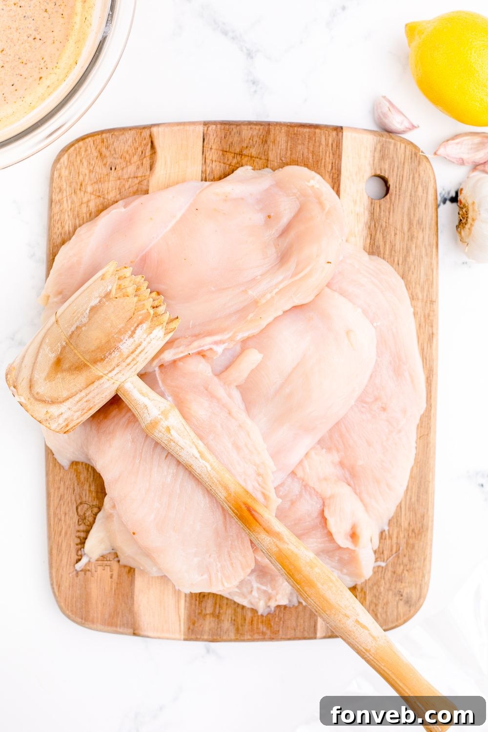 mallet sitting on top of raw chicken on cutting board 