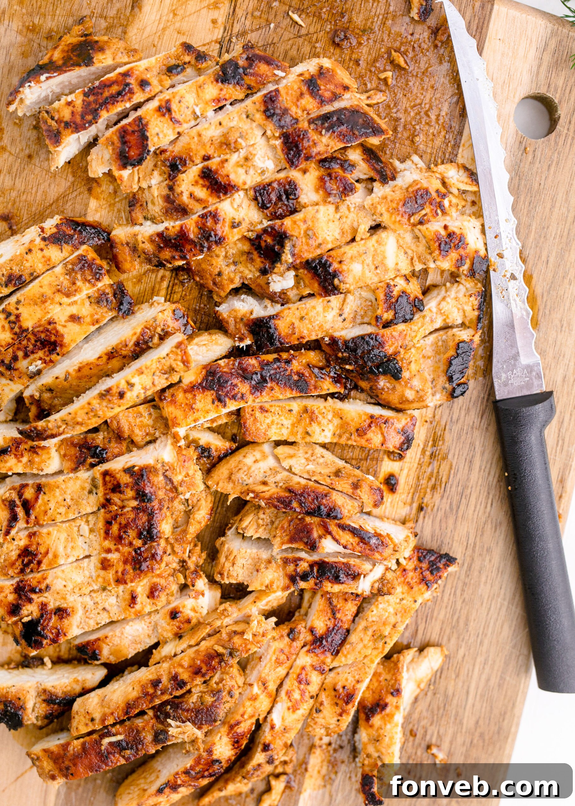 Chicken on a wooden cutting board being sliced up by a sharp knife