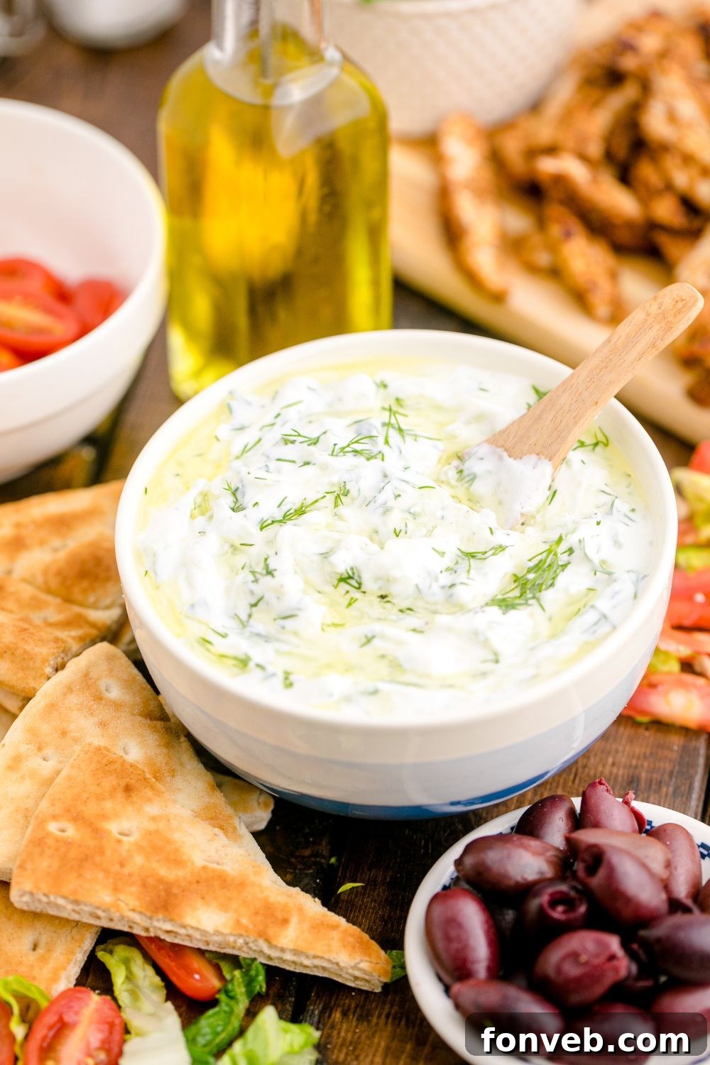 Tzatziki Sauce in a white and blue bowl with a bowl of black olives in front