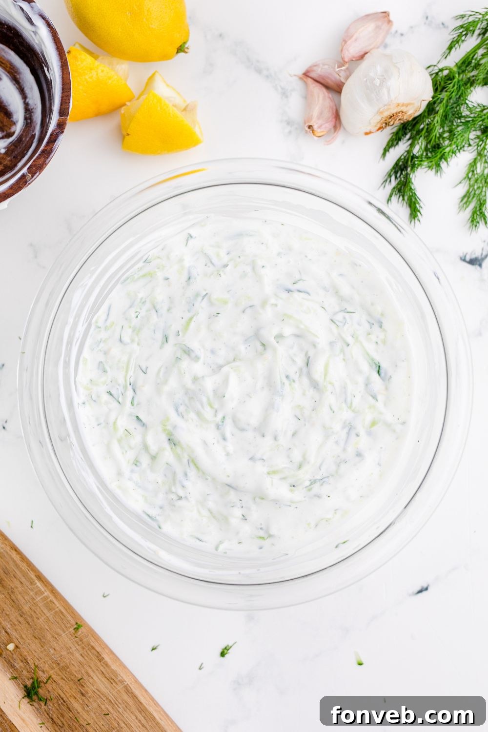 bowl of Tzatziki Sauce on table with garlic and dill by the bowl