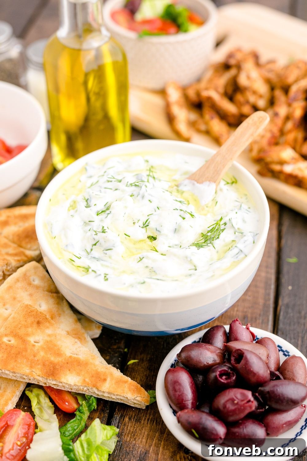 Tzatziki Sauce in a ceramic bowl with pita bread, olives and more around the bowl for dipping