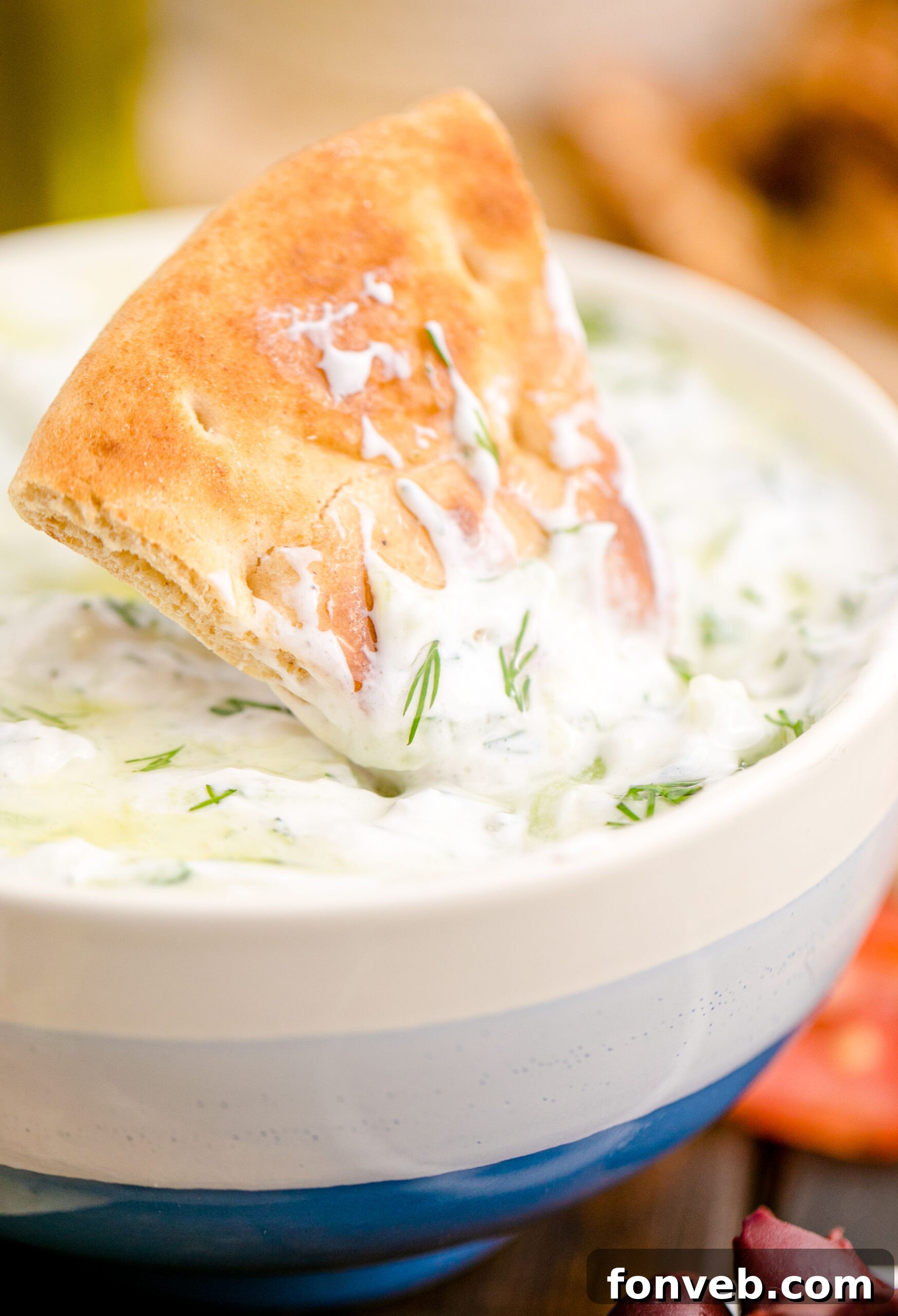 Tzatziki Sauce in a white and blue bowl with a sauce covered pita chip being dipped in