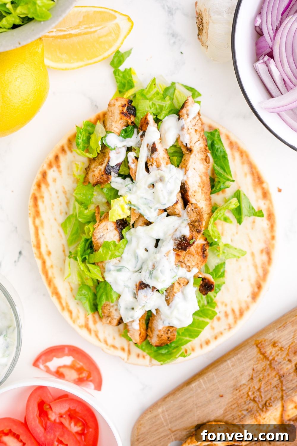 Tzatziki Sauce on a gyro on table with sliced tomatoes and onions to the side