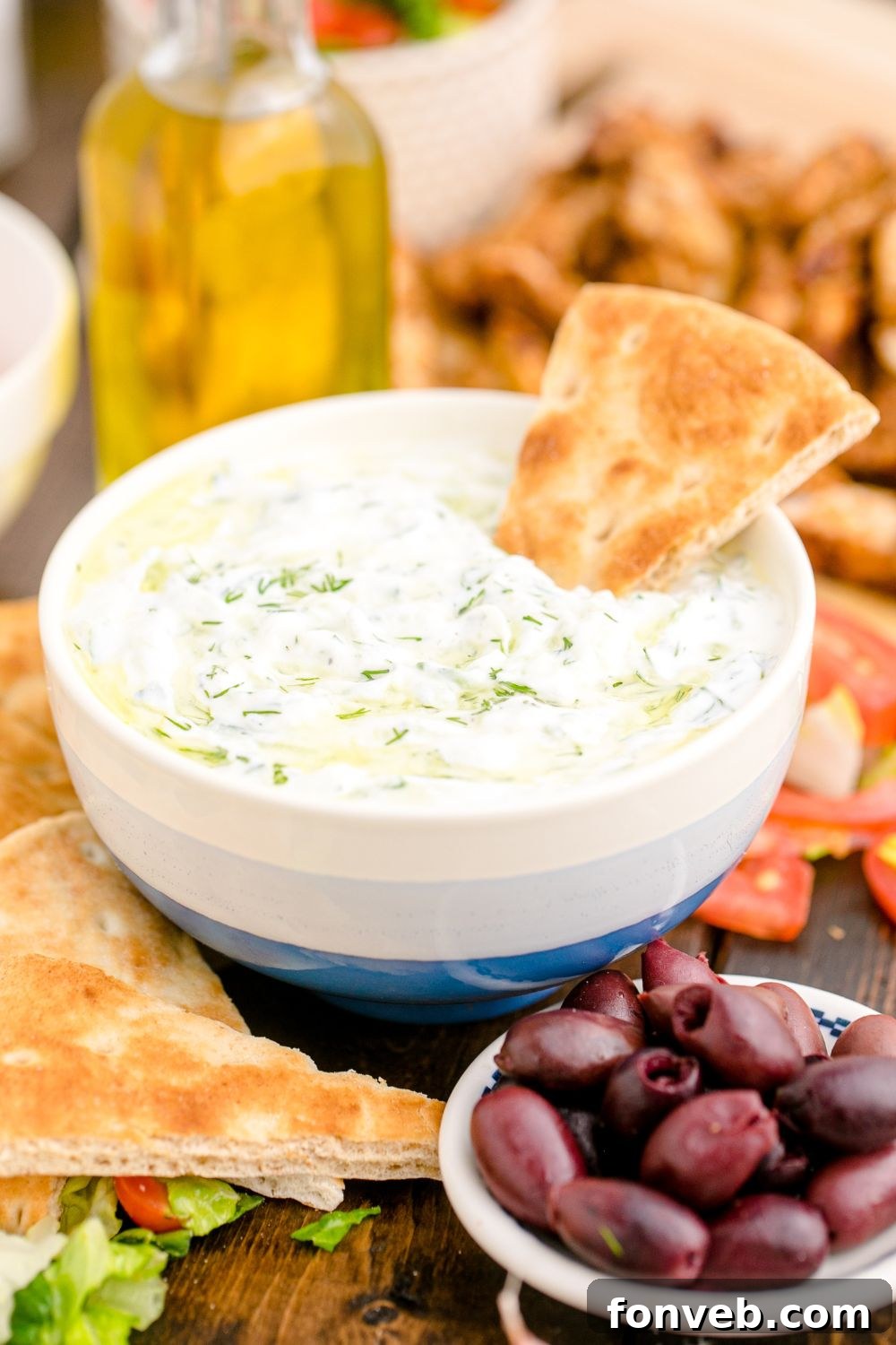 Tzatziki Sauce in a white and blue bowl with a bowl of black olives in front