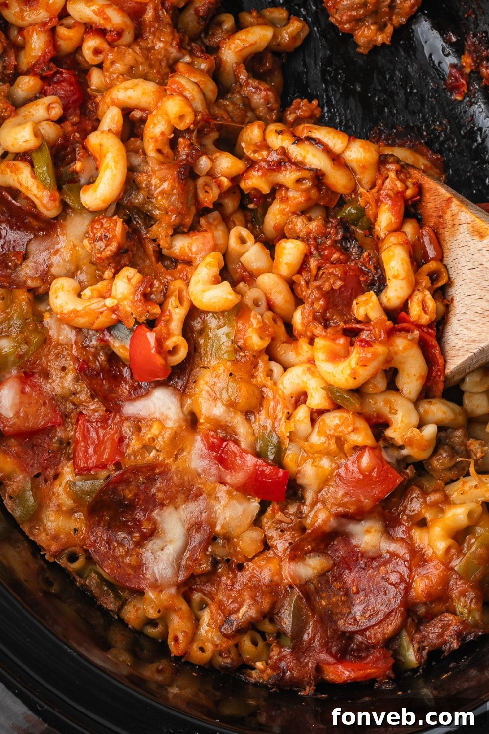 crockpot with pizza casserole inside of it with a wooden spoon in container