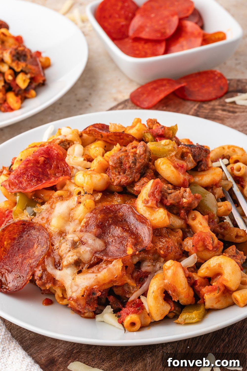 plate full of cheesy pepperoni pasta with a bowl of pepperonis to the side