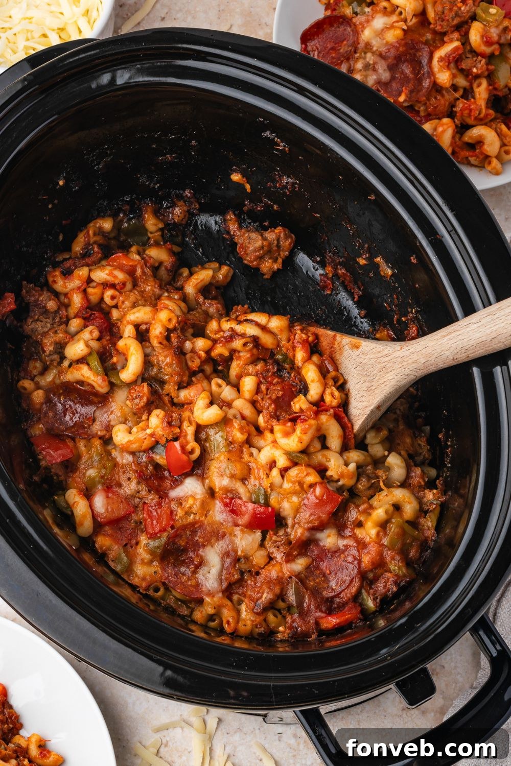 overhead Slow Cooker Pizza Casserole in a slow cooker on table with a spoon to side of container