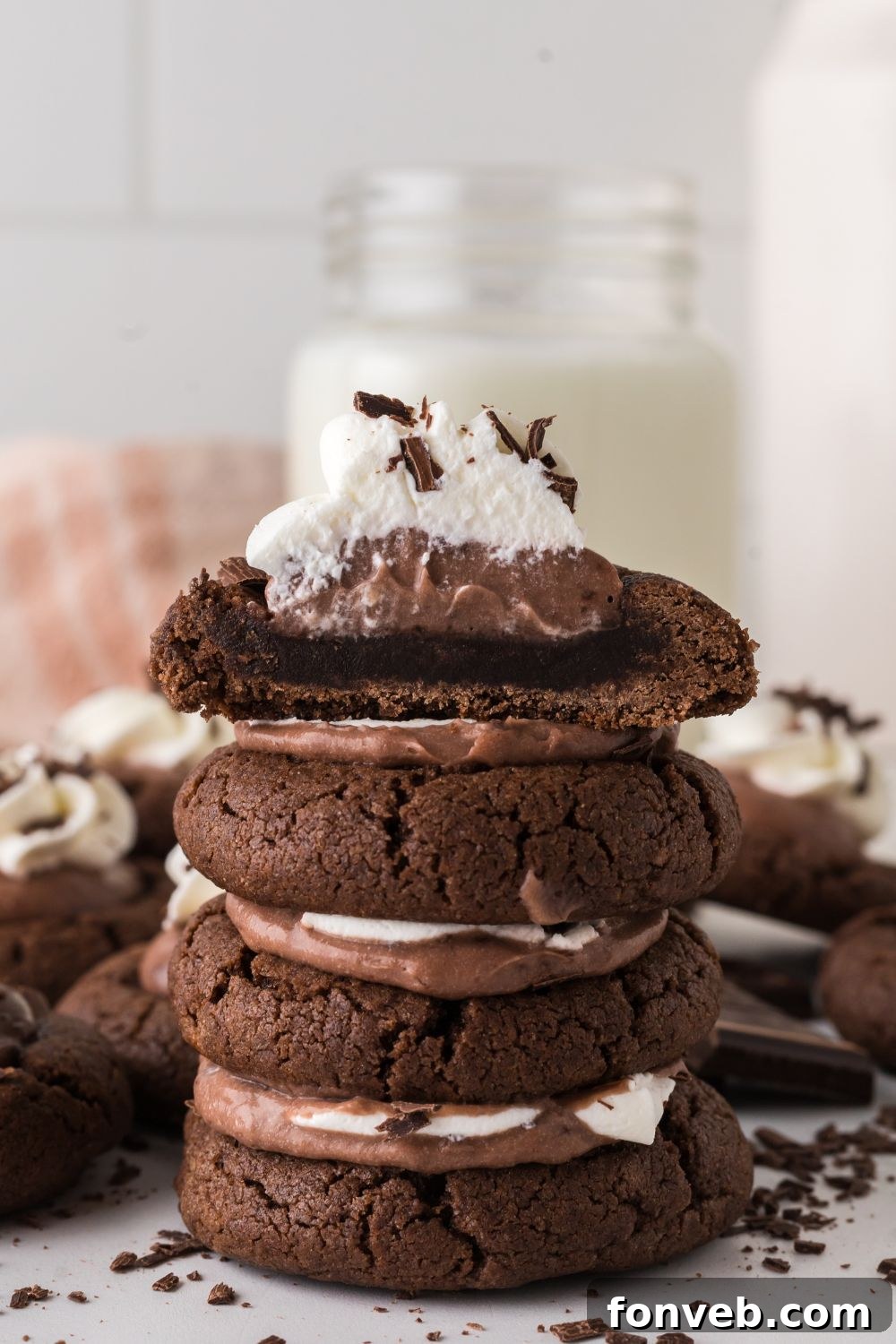 A stack of gourmet Chocolate Pie Cookies, with one elegantly cut in half, revealing the luscious layers of fudgy cookie, smooth chocolate pudding, and airy whipped cream.