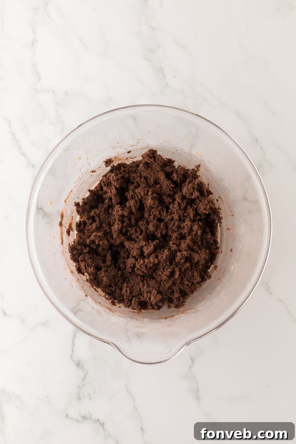 A bowl brimming with rich, dark chocolate cookie batter, perfectly poised on a kitchen table, ready for baking.