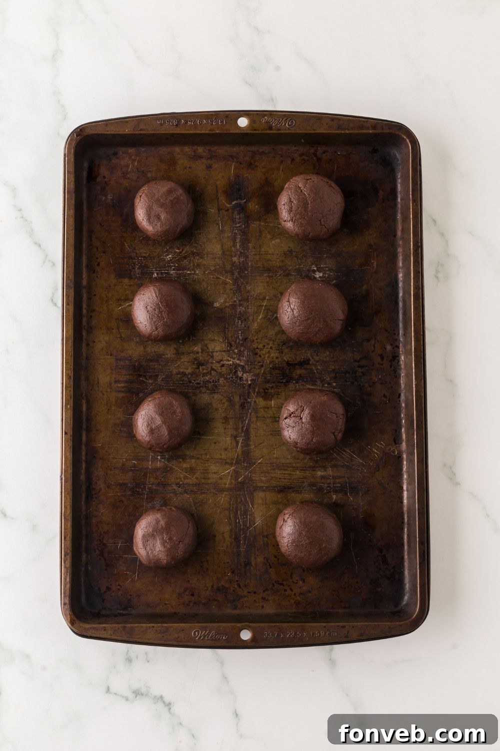 A baking tray neatly arranged with evenly spaced, perfectly rounded chocolate cookie dough balls, awaiting their transformation in the oven.