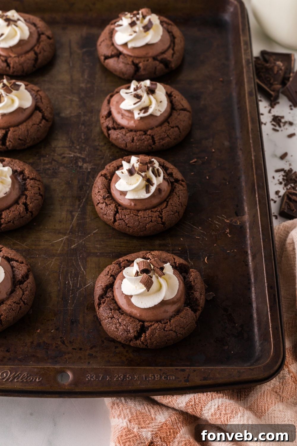 A freshly baked cookie tray featuring the finished Chocolate Pie Cookies, each elegantly topped with a swirl of whipped cream and delicate chocolate shavings, a true visual feast.