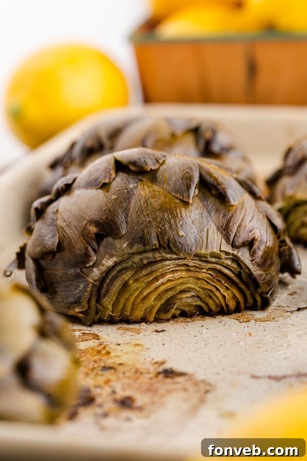 side view of artichokes in a baking tray with lemons to the side