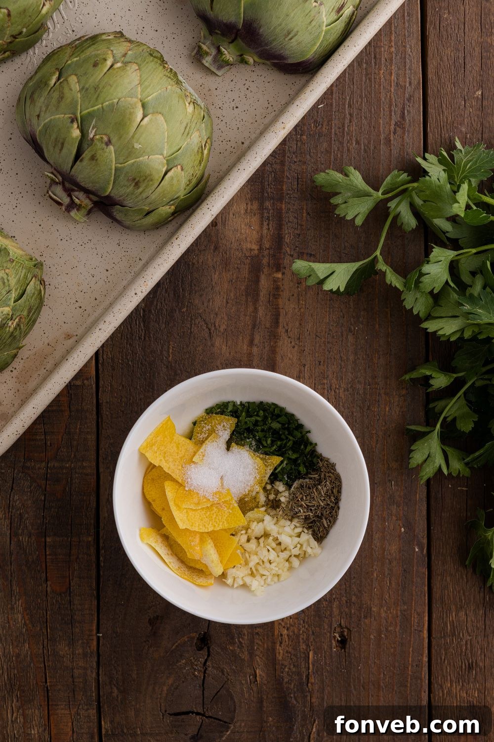 Oven Roasted Artichokes on a baking tray with a bowl of spices and lemon to season