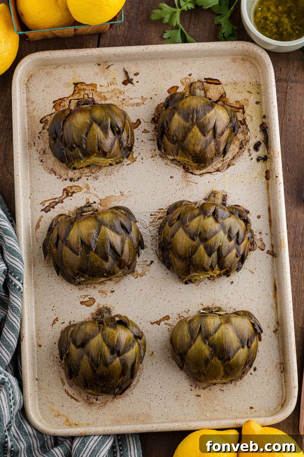 oven roasted artichokes on a baking tray with lemons around it