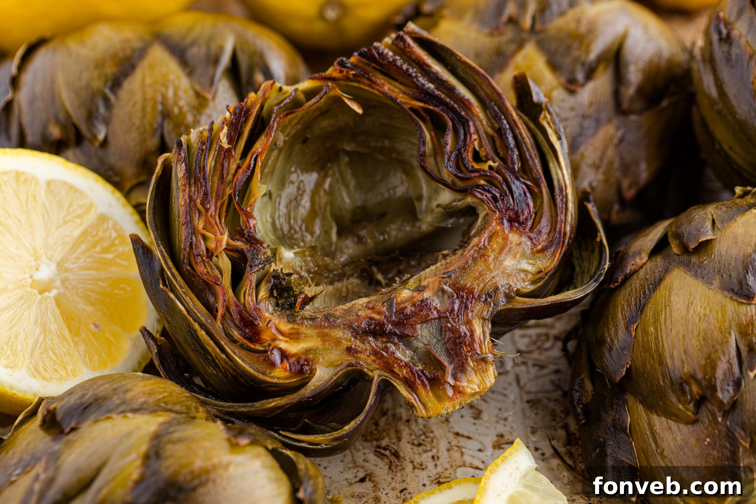 up close shot of a roasted artichoke on a plate with sliced lemons
