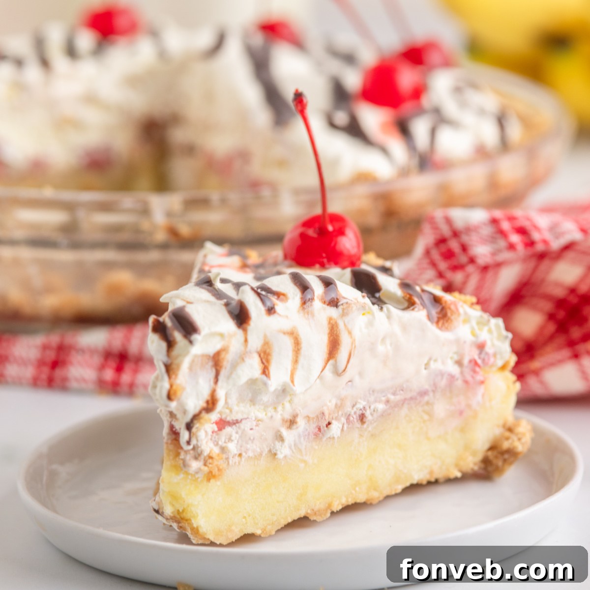 A vibrant slice of No Bake Banana Split Pie on a white plate, topped with a glistening cherry and delicate fudge drizzle.