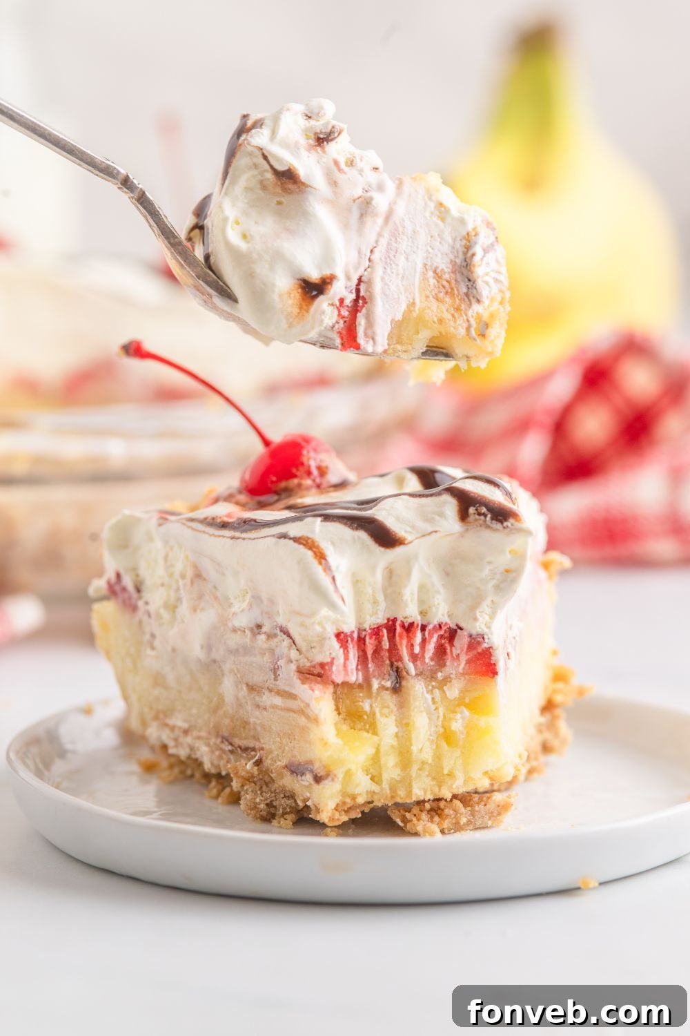 A pristine white plate holding a perfect slice of No Bake Banana Split Pie, with a bite playfully taken out of it.