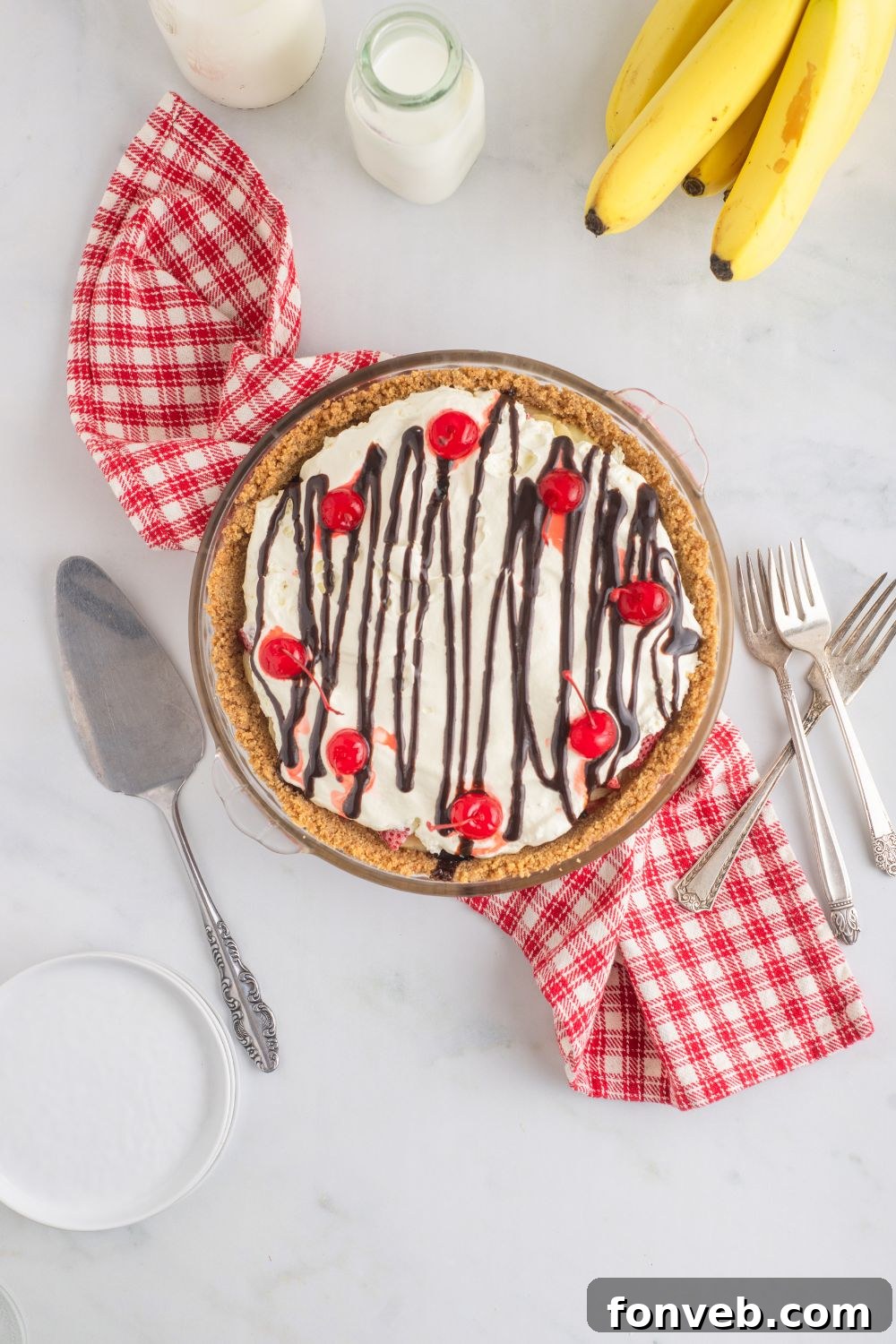 A No Bake Banana Split Pie showcased on a table, surrounded by forks, a pie scoop, and other serving essentials, creating an inviting spread.