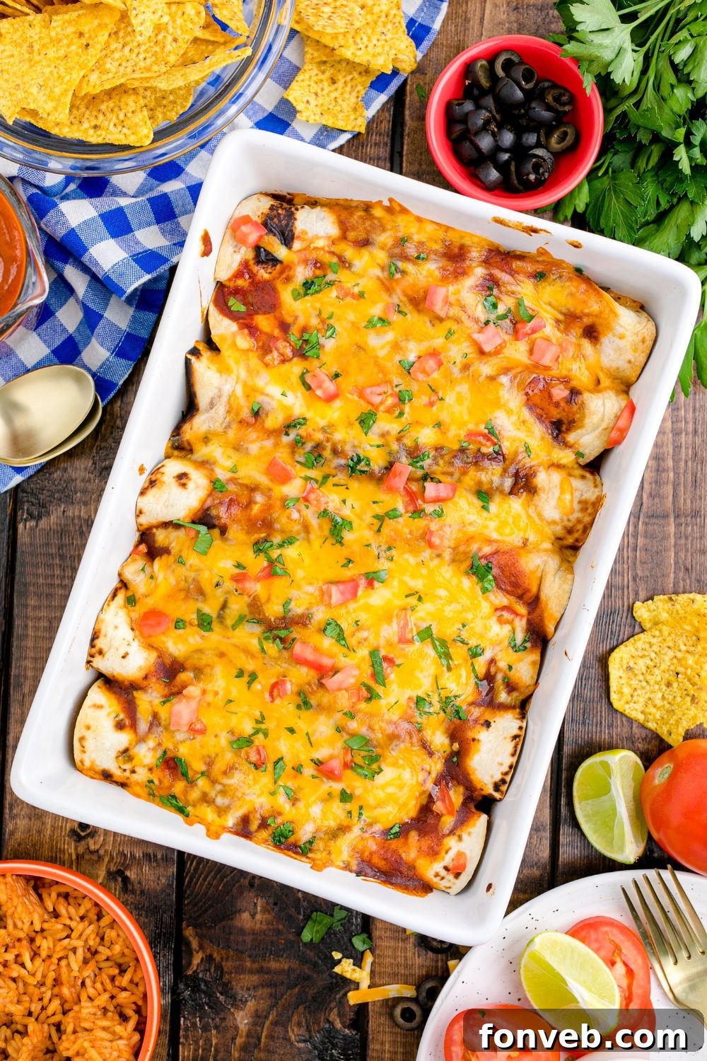overhead picture of a casserole dish full of enchiladas on table. Condiments and ingredients in bowls on table around the pan 