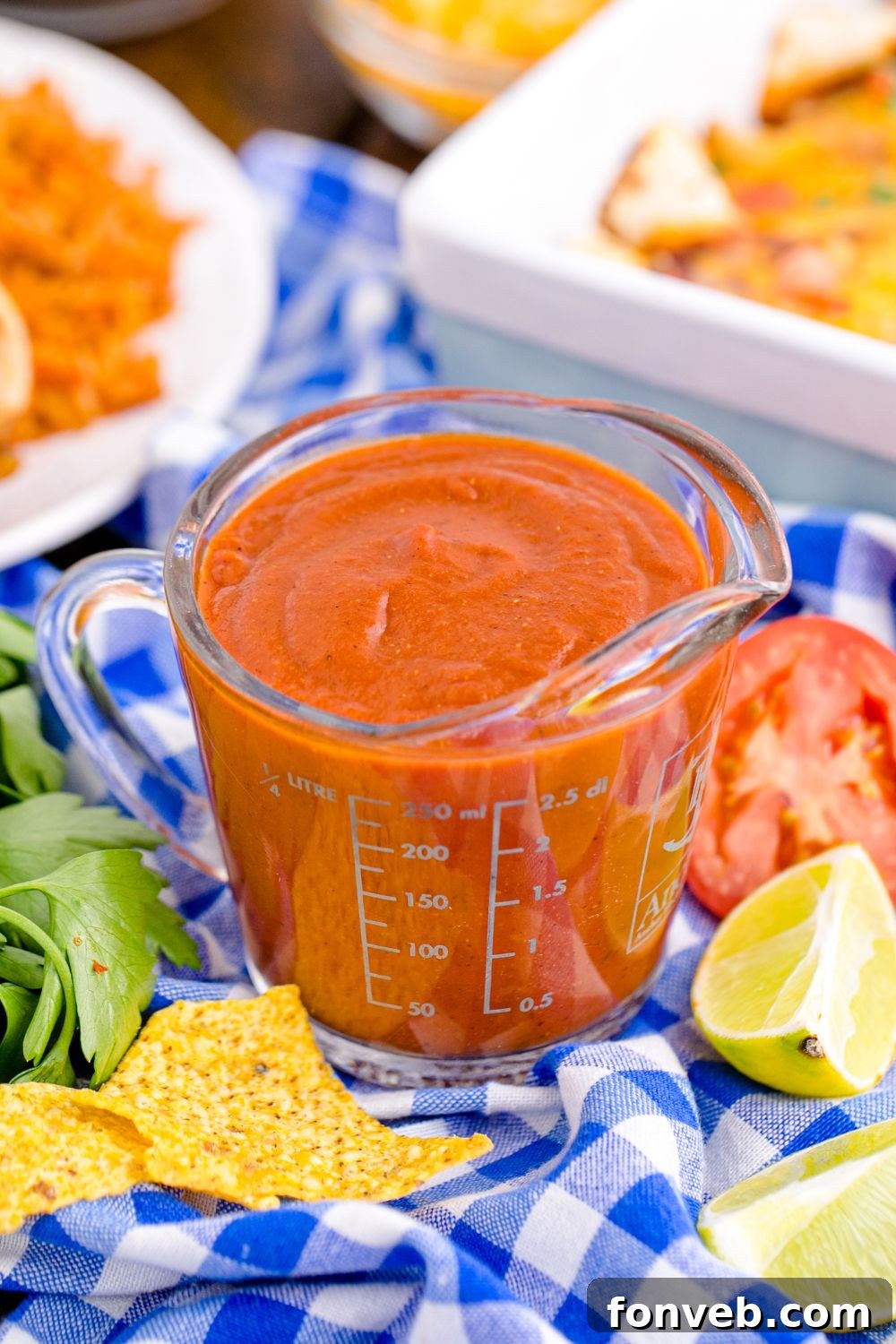 glass container of homemade enchilada sauce in it with a plate of enchiladas the side