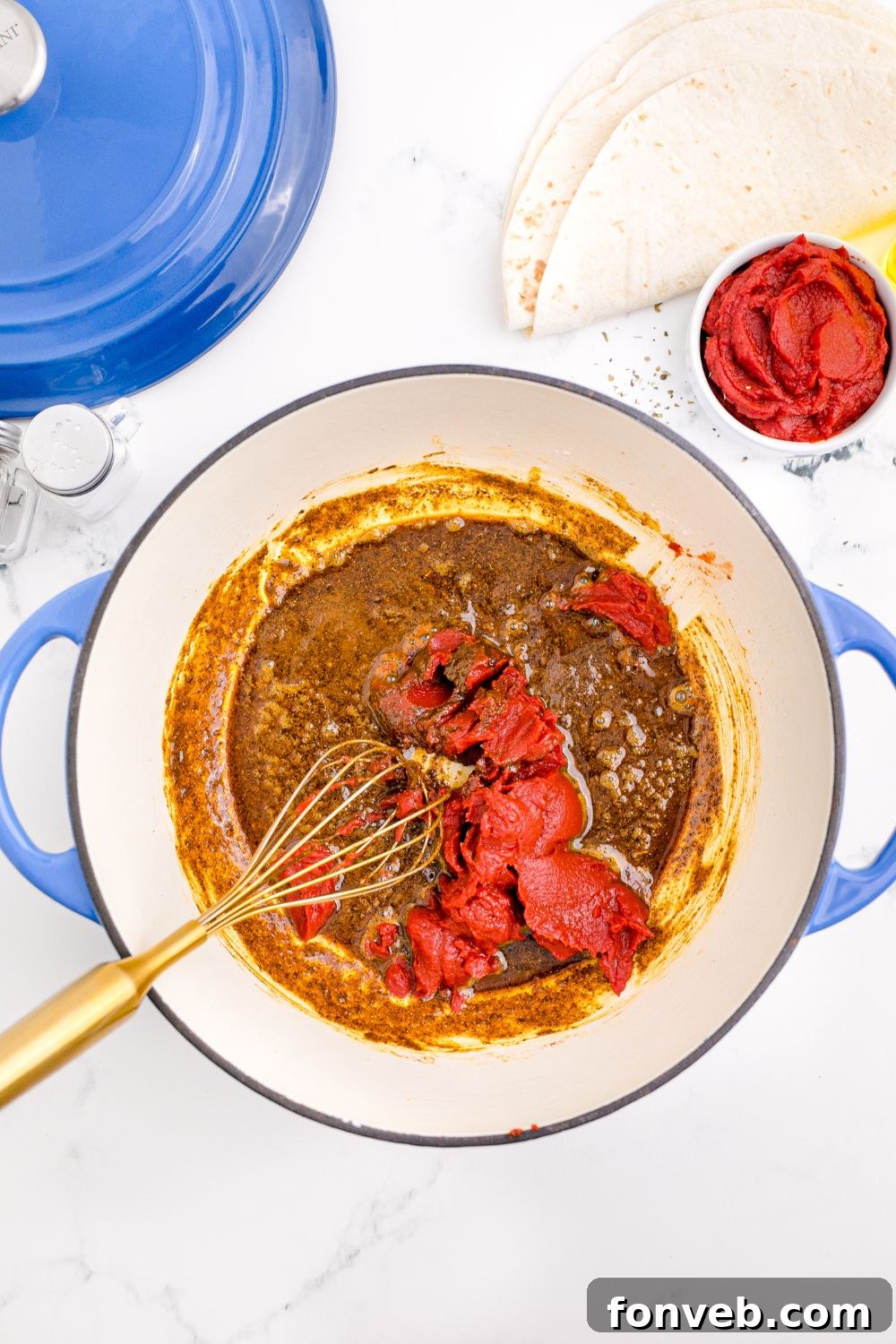 a whisk mixing up tomato paste in a pot on table for making Homemade Enchilada Sauce
