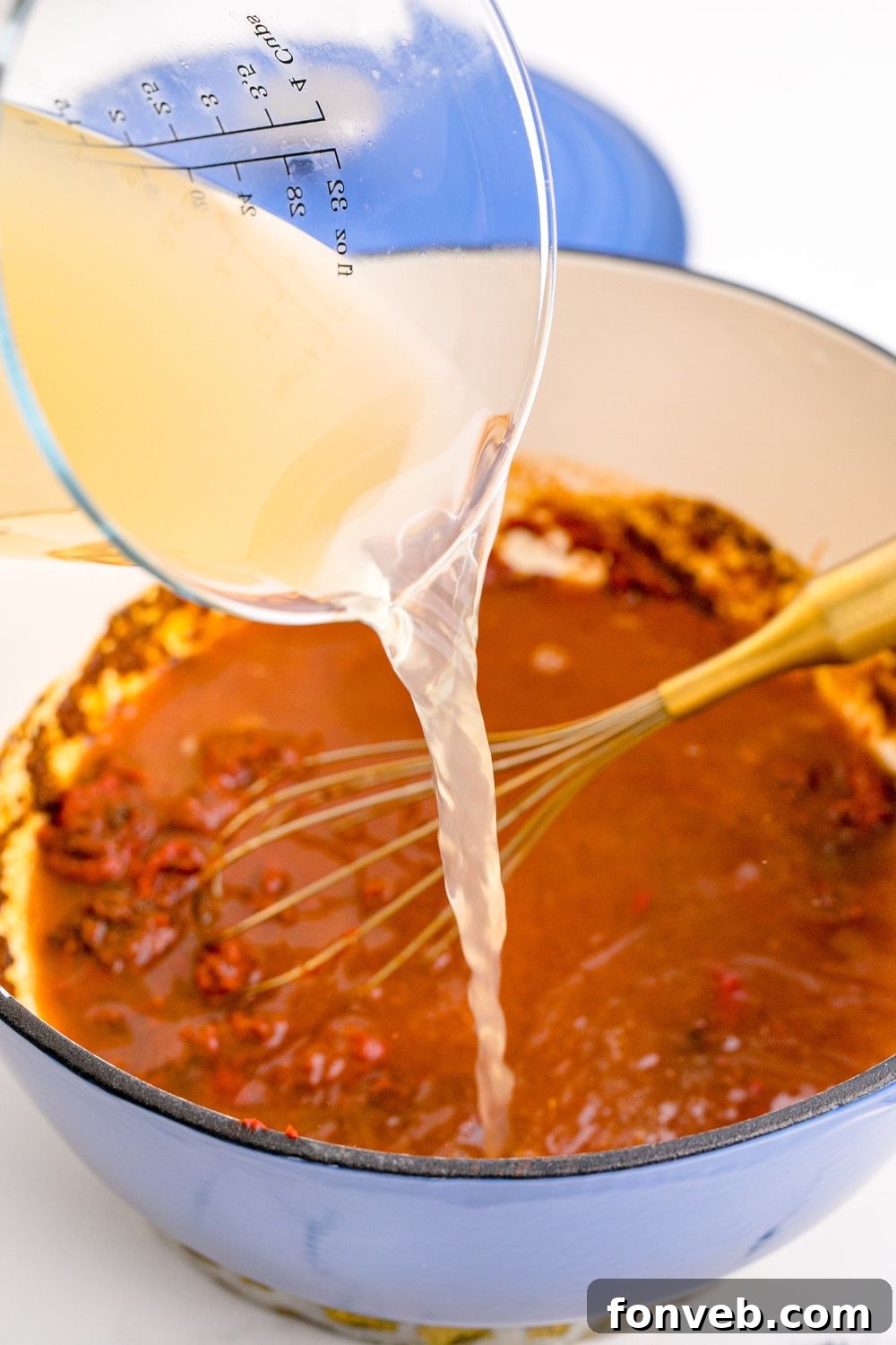 Homemade Enchilada Sauce being made with stock being poured into pan with tomato mixture in it