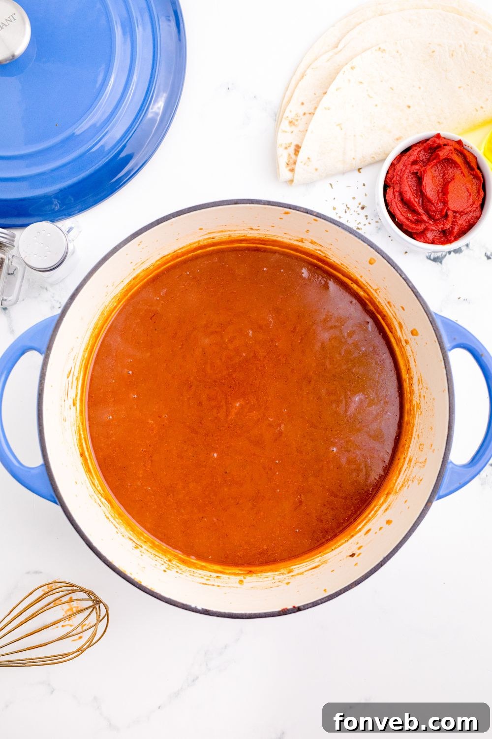 Homemade Enchilada Sauce in a pot sitting on table with whisk to the side of pan
