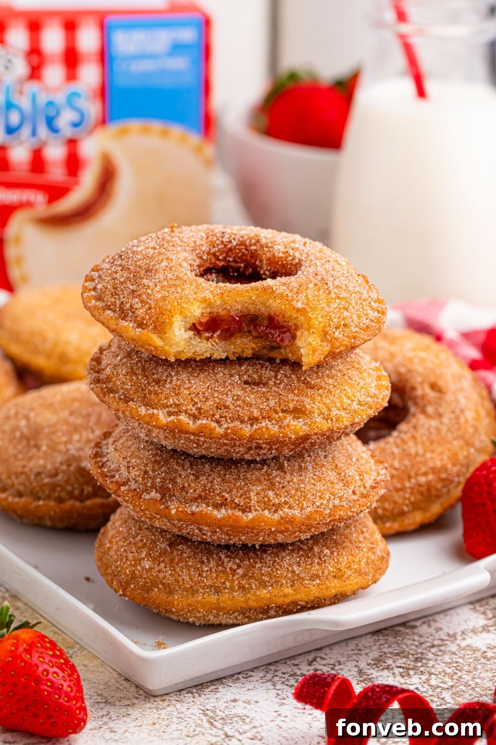 stack of fried uncrustables on plate with more behind it and a tall glass of milk and uncrustable box behind it on table