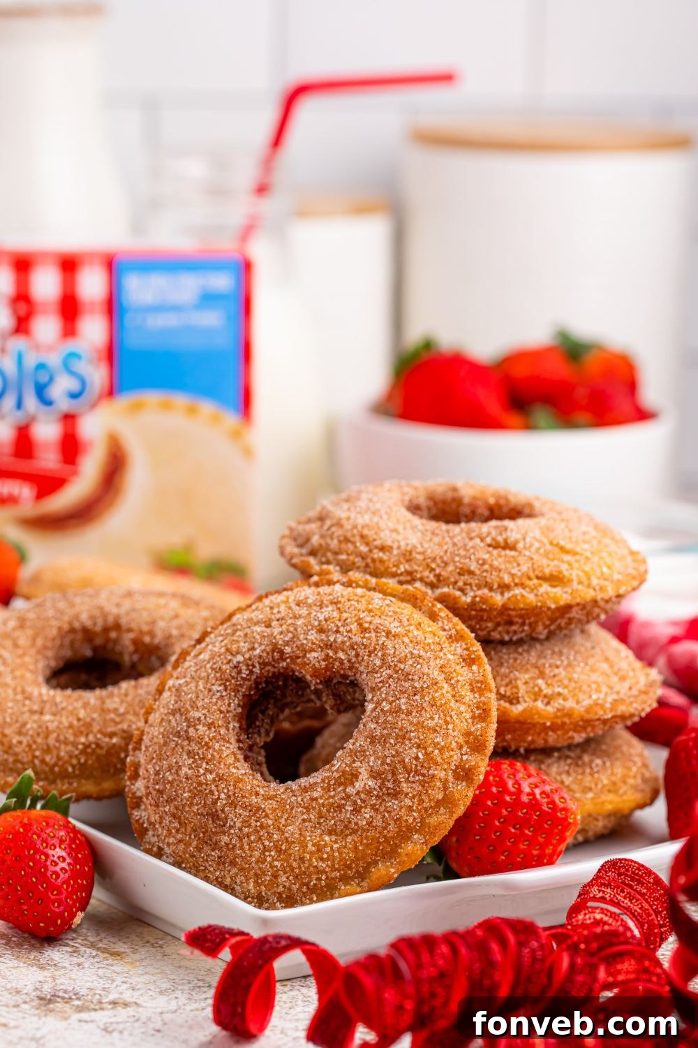 Fried Strawberry Uncrustables stacked on plate and placed around with some strawberries in a bowl behind plate and a glass of milk with straw 
