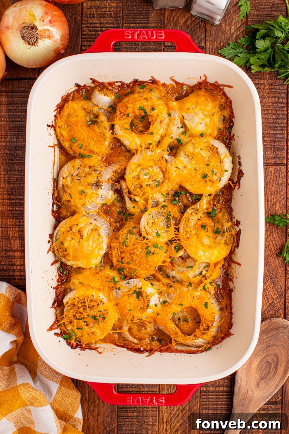overhead look of Cheesy Tennessee Onions in a pan on table with parsley and onions around the table 